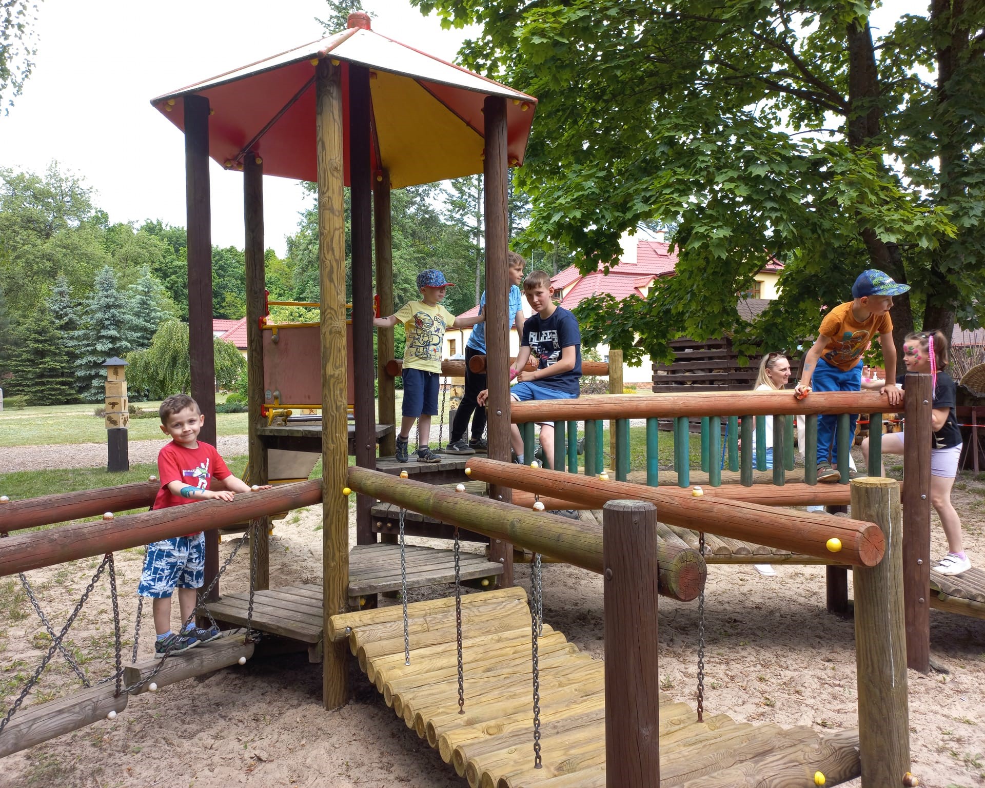 Zdjęcie przedstawia grupę dzieci na drewnianej konstrukcji placu zabaw